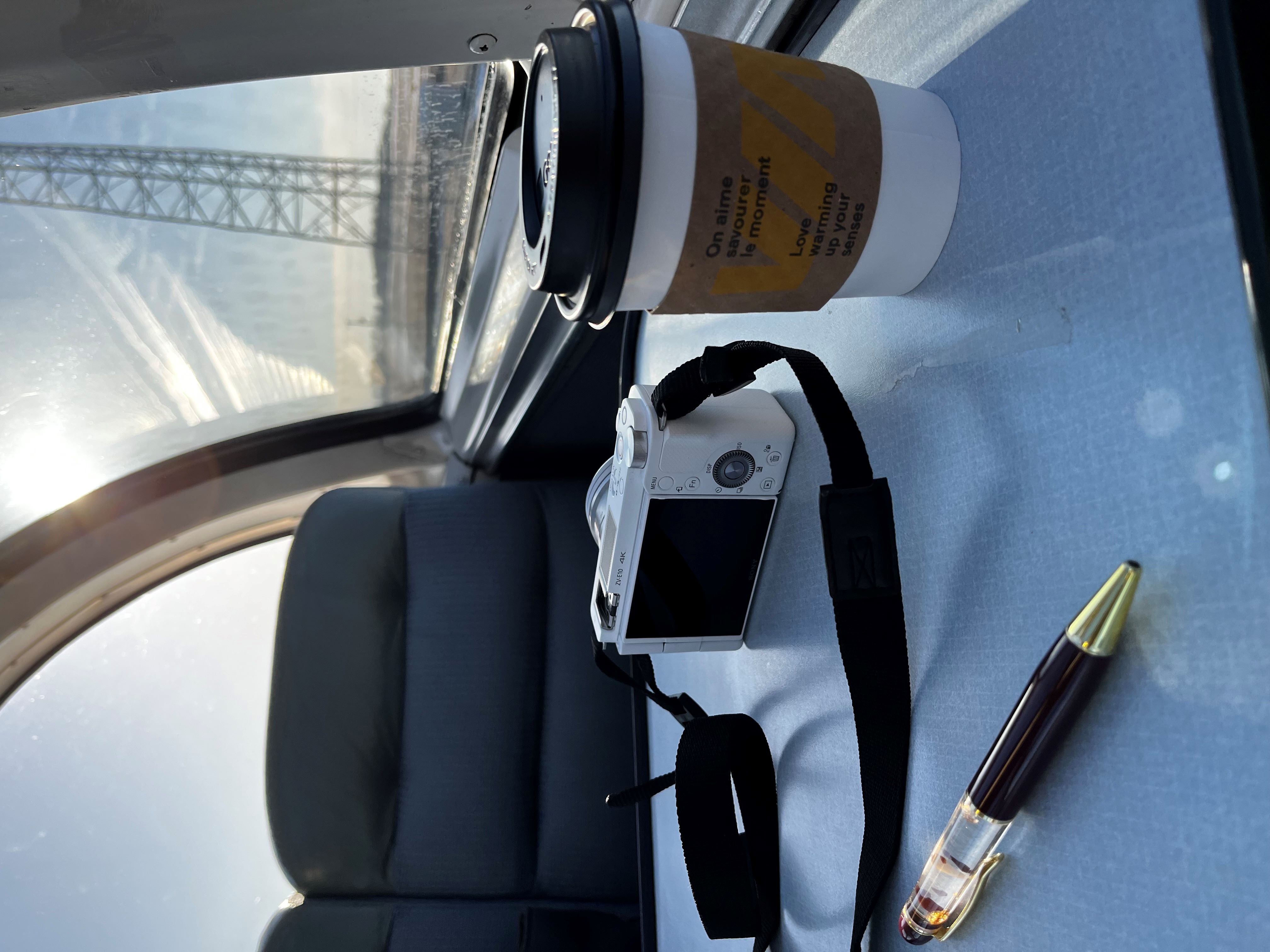 Photo of a pen, a camera, and a cup of coffee on a table inside of a VIA Rail train taken by a Canoo user.