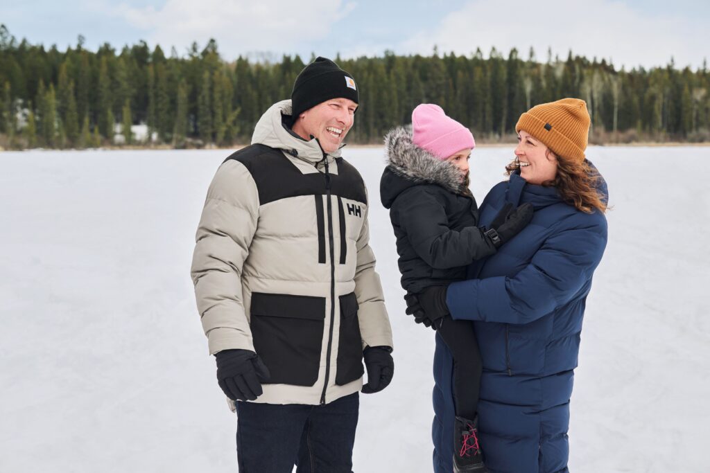 Family wearing winter jackets in front of a snowy background.