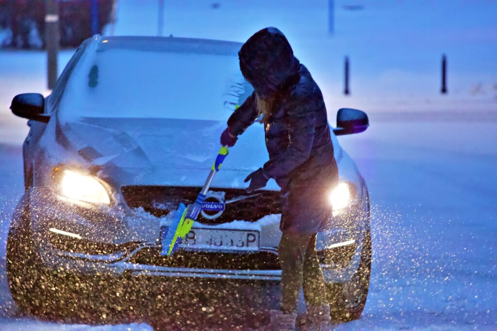 Someone brushing the snow of their car during winter.