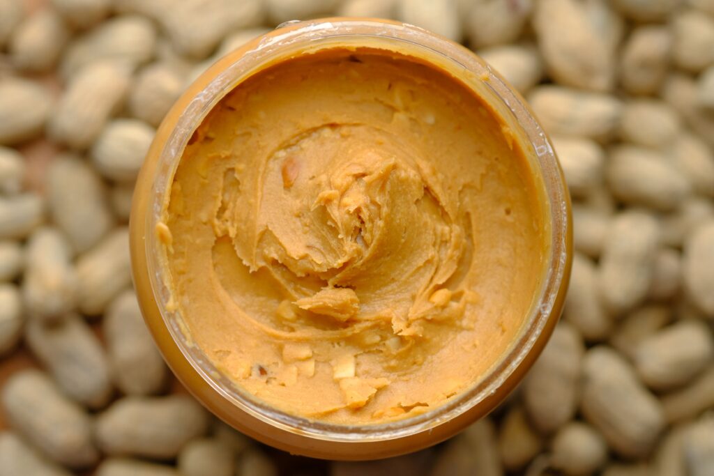 A jar of peanut butter on top of a pile of peanuts.